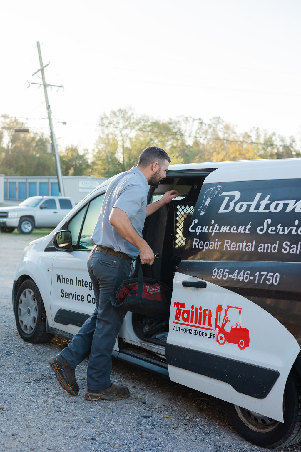Bolton Equipment Services field tech loading tools into the branded Tailift Authorized Dealer service van